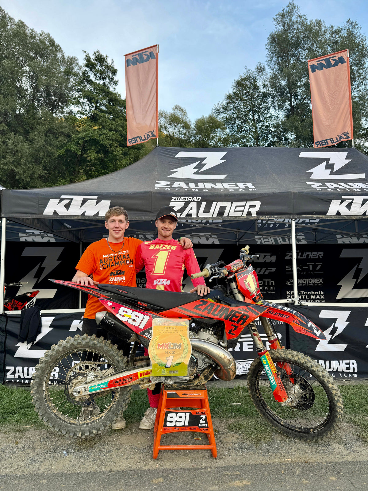 Manuel Gumpenberger und Marvin Salzer neben der #991 unter dem Zelt des Zauner Racing Teams, mit der Plakette Österreichischer Staatsmeister MX2 2026